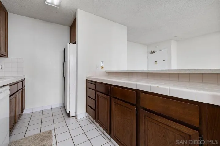 The other side of the kitchen has more cabinets and drawers under the large counter opening up to the entry area. The refrigerator is tucked back at the end of the kitchen.