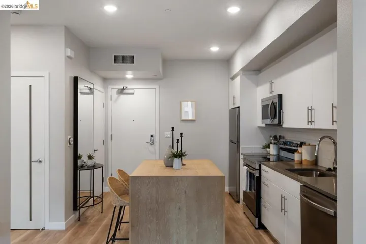 Kitchen with stainless steel appliances, light wood finished floors, white cabinetry, recessed lighting, and a breakfast bar