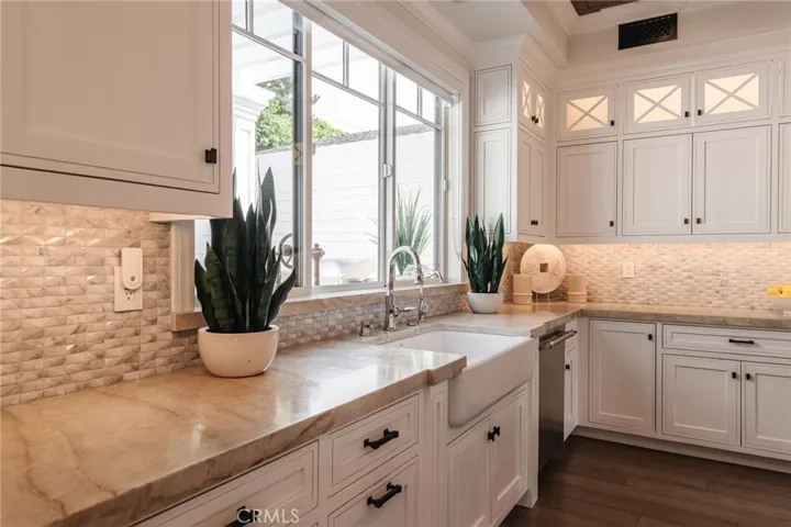Beautiful stone work, tile, farm sink and under cabinet/top cabinet lighting customize this kitchen