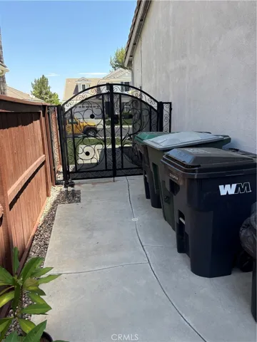 West Side of House & Wrought Iron Gate with Trash Bins Storage.