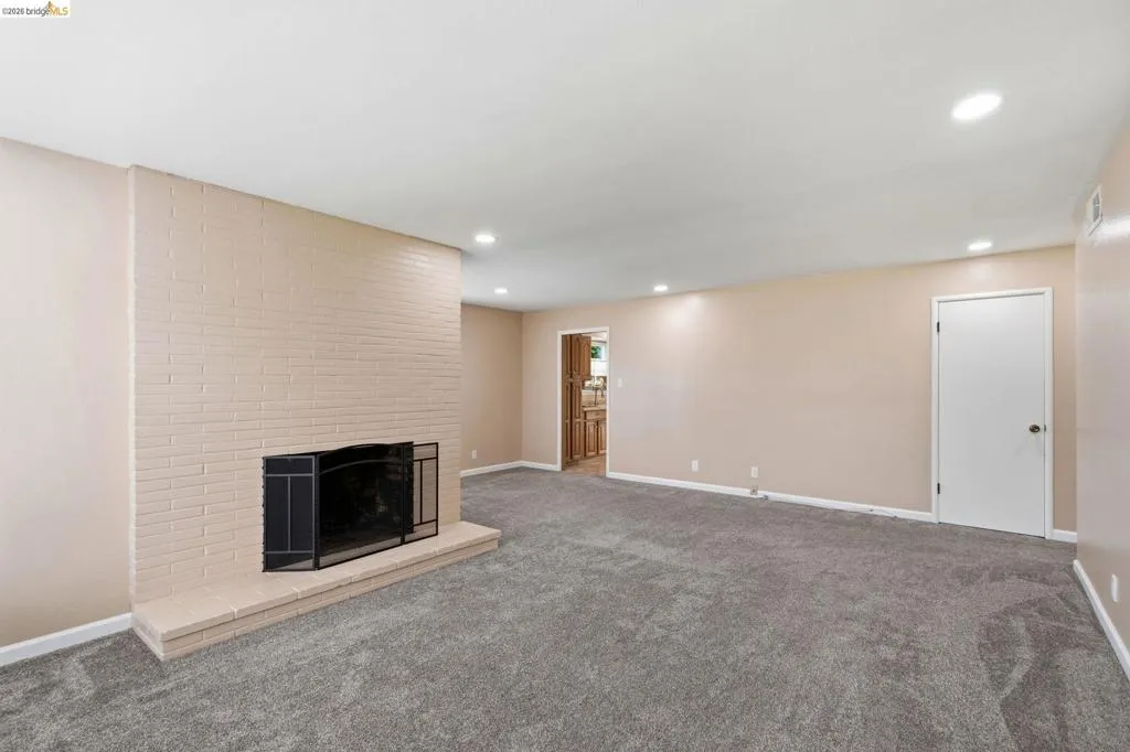 Spacious room featuring a painted brick fireplace with hearth, recessed lighting, neutral wall tones, and plush carpet flooring