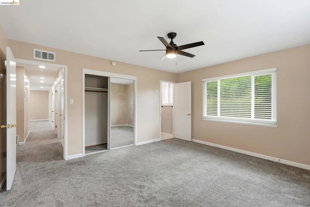 Bedroom featuring soft gray carpeting, a multi-pane window with horizontal blinds, and a ceiling fan with integrated lighting