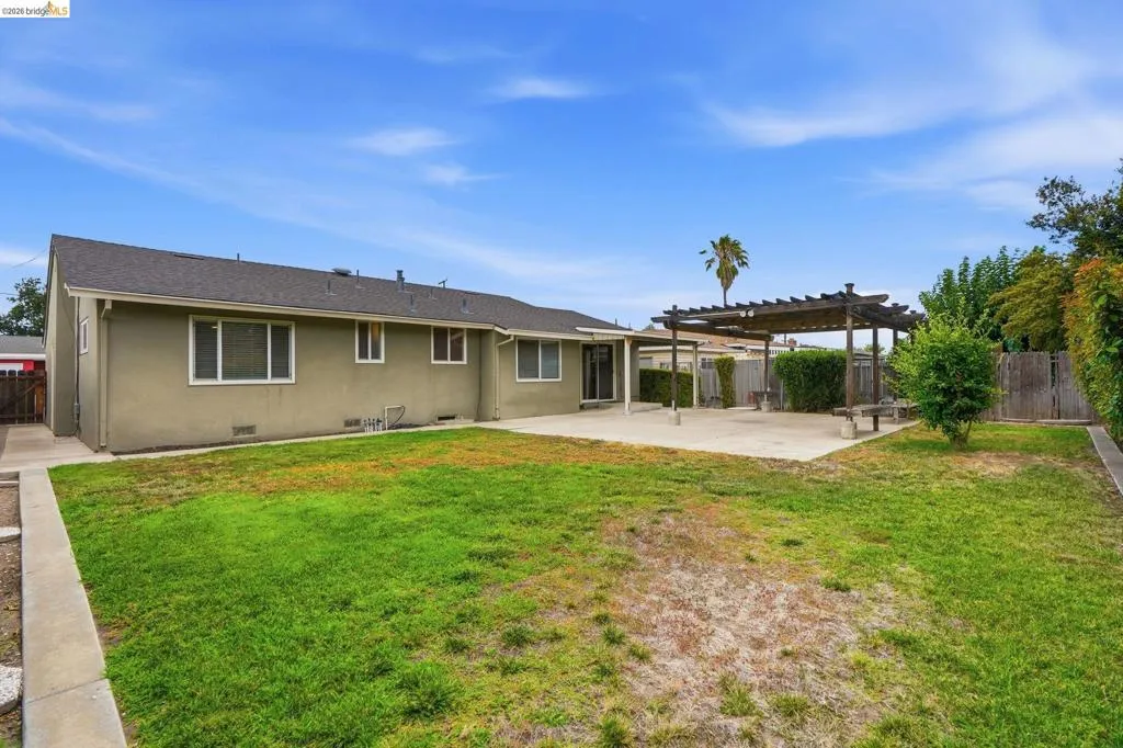 Expansive backyard featuring a concrete patio, a wooden pergola structure, a grass lawn, and perimeter fencing