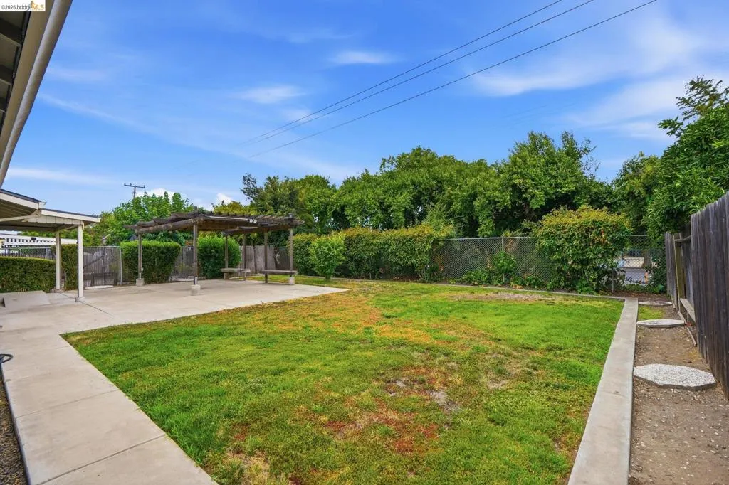 Expansive backyard featuring a large concrete patio, a wooden pergola structure, and a lawn area