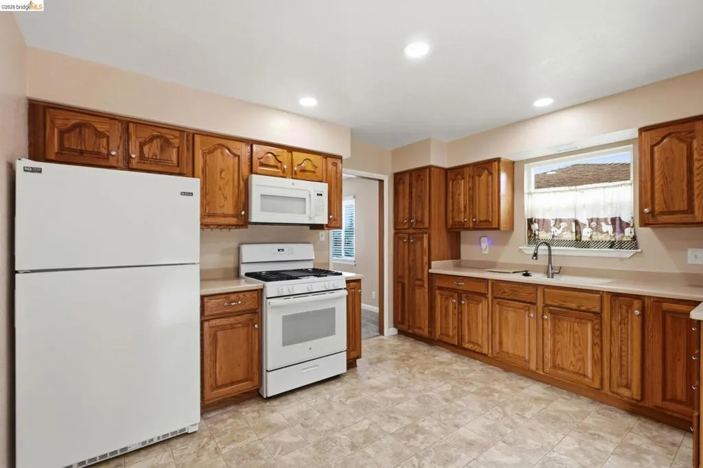 Kitchen featuring extensive wood cabinetry, white appliances, a window above the sink, recessed lighting, and tile flooring
