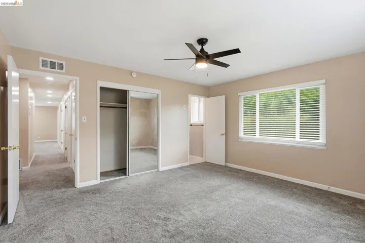 Bedroom featuring soft gray carpeting, a multi-pane window with horizontal blinds, and a ceiling fan with integrated lighting