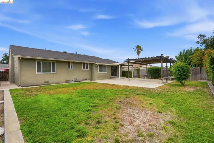 Expansive backyard featuring a concrete patio, a wooden pergola structure, a grass lawn, and perimeter fencing