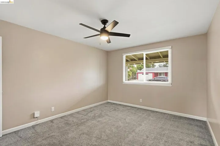 Neutral tone walls, grey carpet flooring, white trim, a multi-pane window with white blinds, and a ceiling fan with integrated lighting