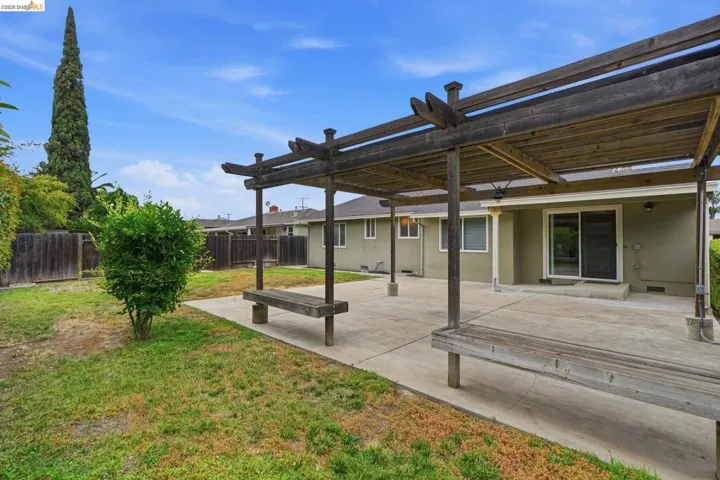 Expansive backyard featuring a concrete patio, a pergola with built-in wooden benches, and a sliding glass door leading into the home