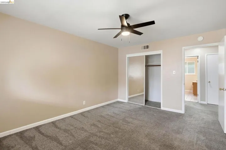 Neutral-toned room featuring a dark ceiling fan, gray carpet flooring, mirrored closet doors, and white trim