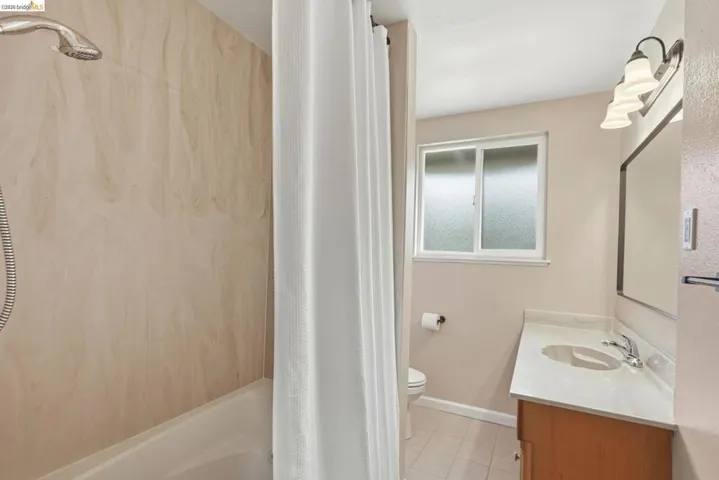 Bathroom featuring a shower-tub combination with a handheld showerhead, light-toned wall paneling, a single vanity with an integrated sink, a large mirror, and a frosted glass window