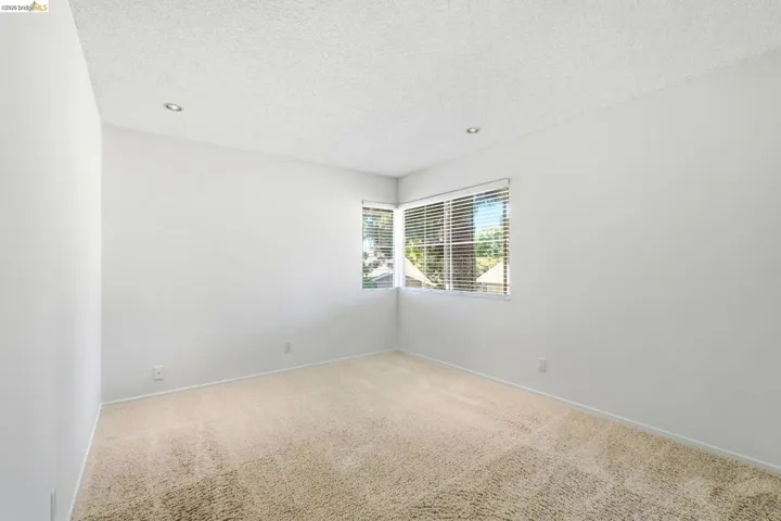 Carpeted room featuring recessed lighting, a corner window with horizontal blinds, and white walls
