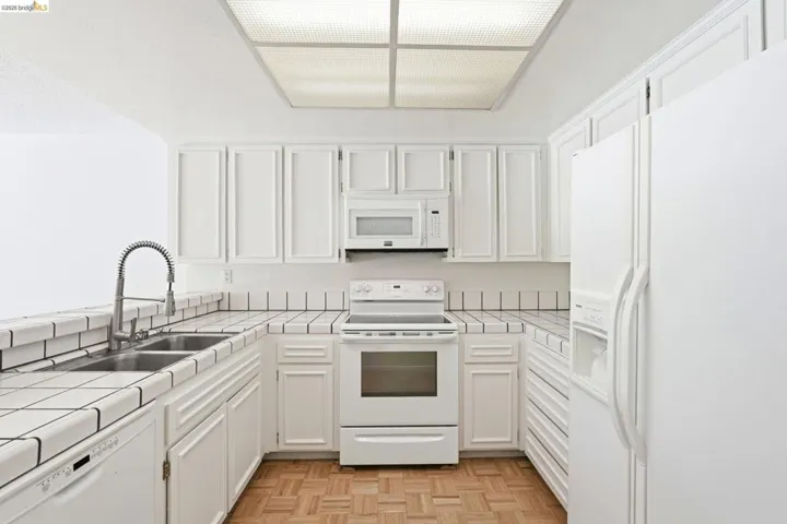 U-shaped kitchen featuring white cabinetry, tile countertops and backsplash, integrated white appliances, and a basketweave wood-finish floor