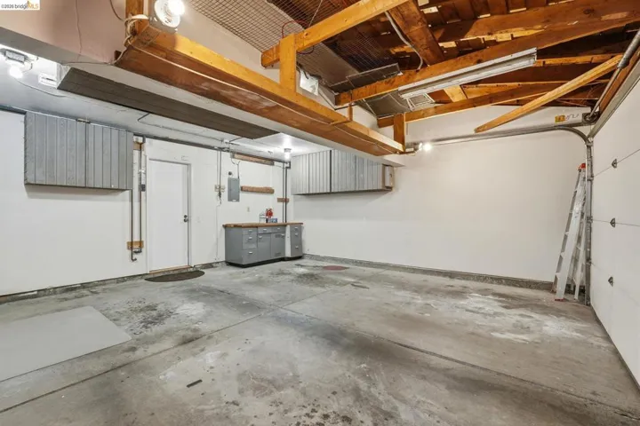 Spacious garage featuring a concrete floor, exposed wood beam ceiling, built-in cabinetry, workbench, and overhead lighting