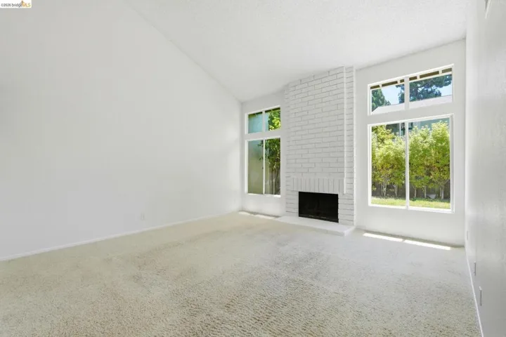 Spacious room featuring vaulted ceilings, a prominent white brick fireplace, and extensive windows