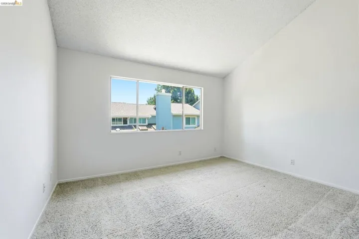 Spacious room featuring vaulted ceilings, a large paneled window, light-colored carpeting, and crisp white walls