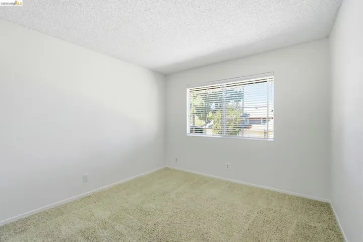 Bright interior room featuring a large window with horizontal blinds, neutral wall paint, and textured ceiling finish