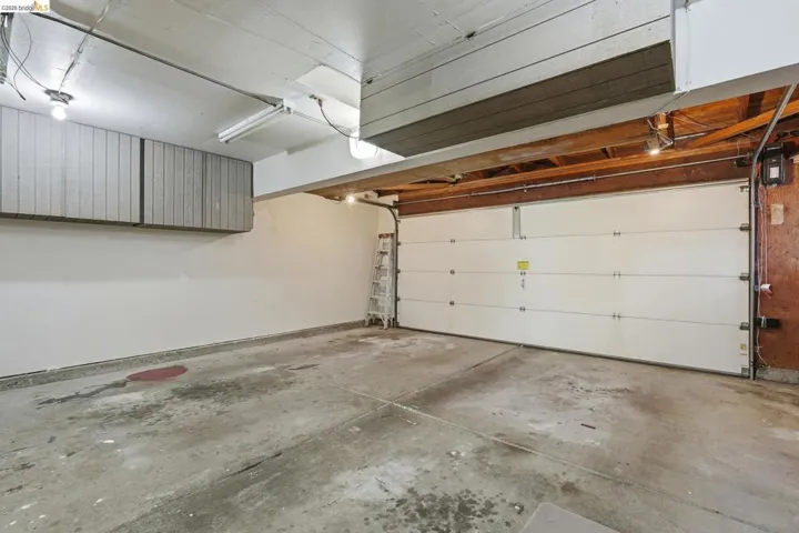 Garage featuring concrete flooring, white walls, overhead lighting, and built-in upper cabinetry for storage