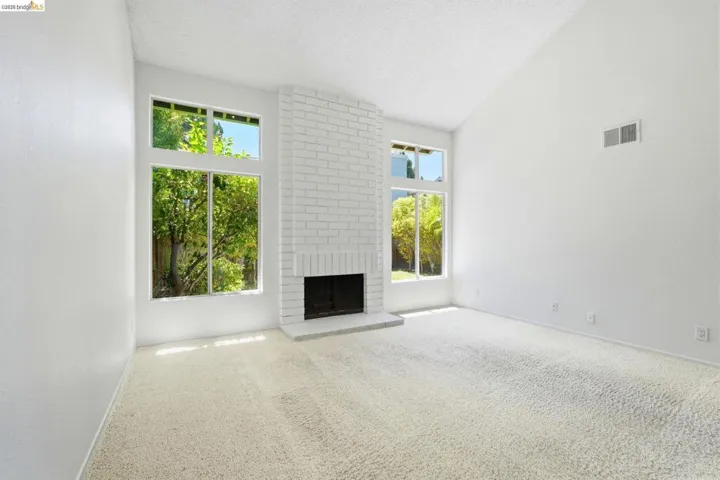 Vaulted ceiling living space featuring a white brick fireplace, broad hearth, and tall windows
