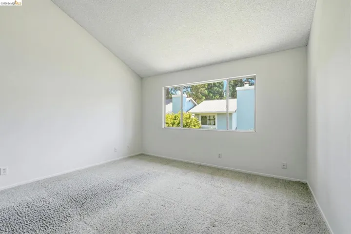 Interior room featuring a vaulted ceiling, light-colored walls, and a large window with white trim