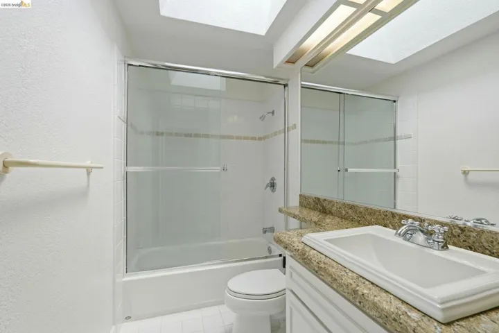 Bathroom featuring a shower-tub combination with sliding glass doors and white tile surround