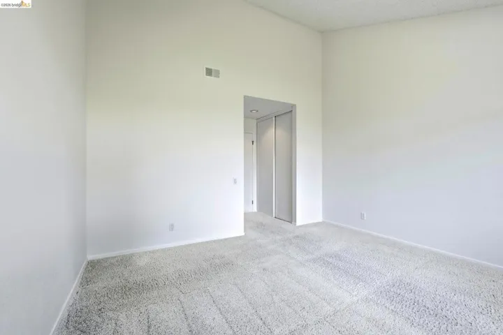 Spacious room featuring vaulted ceilings, light-toned carpeting, and a neutral color palette