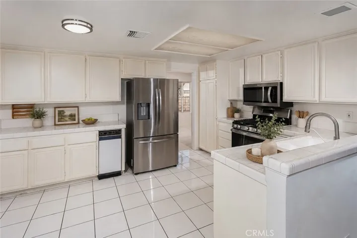 Virtually staged photo. The kitchen opens naturally to the family room and sunny breakfast nook, creating a comfortable everyday gathering space. Features include tile floors and counters, stainless steel appliances, GE® 5-burner gas range, Bosch® silent dishwasher, Whirlpool® microwave, Samsung® refrigerator/freezer, pantry storage, trash compactor, and dual basin sink.