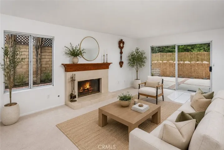 Virtually staged photo. The family room features a gas fireplace, wet bar, dual storage closets, and sliding doors leading directly to the private backyard with tall Cypress trees, raised flowerbeds, lush greenery, brick and concrete patio space, and natural gas hookup for a future BBQ setup. It’s easy to picture movie nights by the fire, holiday gatherings, or slow weekend mornings with the doors open to the backyard while natural light fills the home.