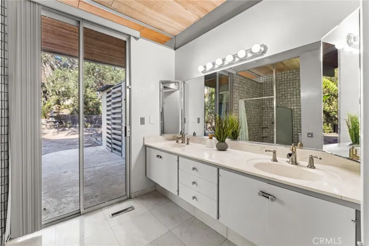 Primary bathroom with dual sinks and sliding doors that lead to private patio