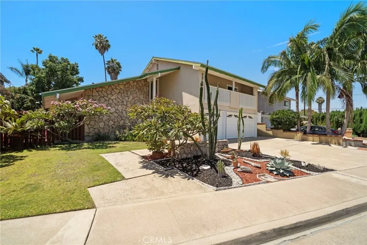 Exceptional curb appeal features a dramatic stone façade, soaring rooflines, manicured landscaping, lush lawn, sculptural succulents, and an oversized driveway