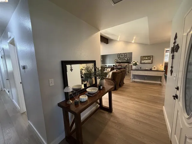Bright entry hall featuring wood-finish flooring, white paneled doors, and vaulted ceilings extending into the main living area