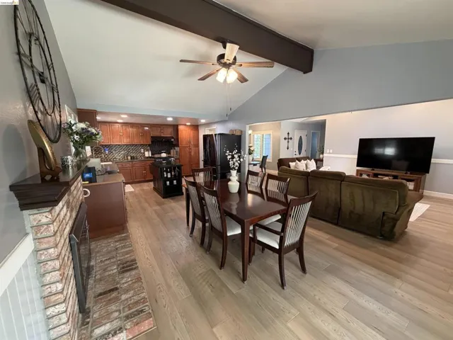 Open-concept living space featuring wood-finish flooring, a vaulted ceiling with exposed beams, and a ceiling fan