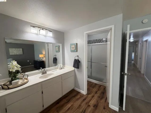 Bathroom featuring a single vanity with an integrated sink, a large wall-mounted mirror, and wood-finish flooring