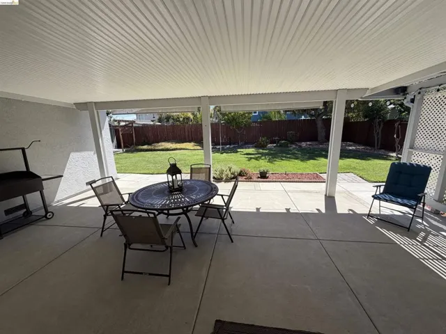 Expansive concrete patio featuring a full-length overhead cover and a manicured lawn