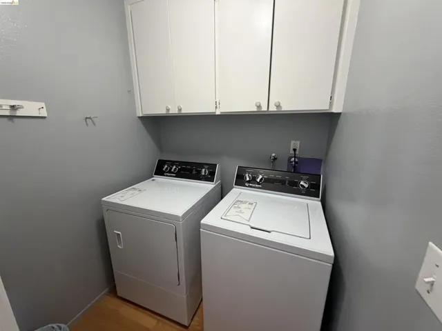 Laundry area featuring upper cabinetry with panel doors and light wood-finish flooring