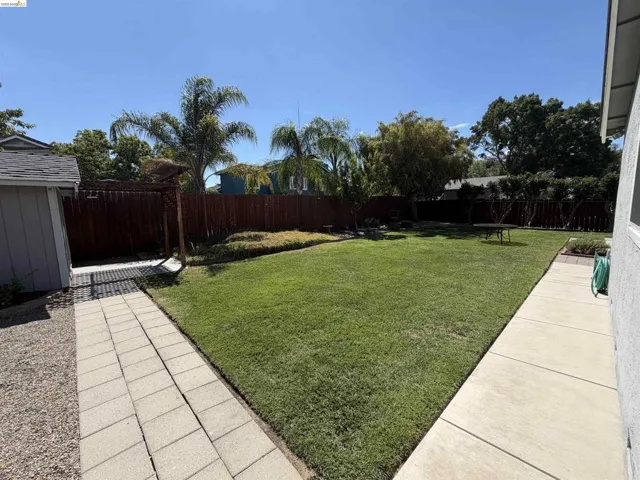 Spacious backyard featuring a large lawn, mature trees, privacy fencing, and a paver pathway