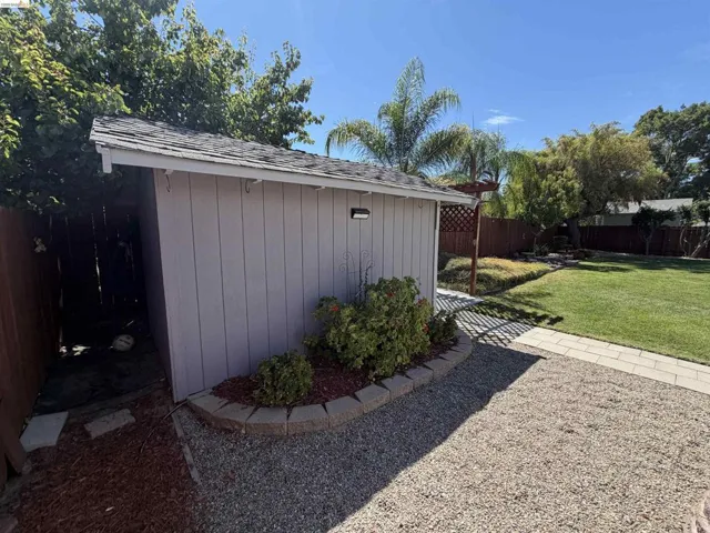 Detached shed with shingle roofing, exterior lighting, and a landscaped base