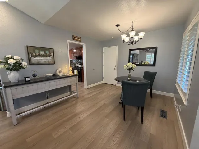 Dining area featuring wood-finish flooring, a contemporary chandelier, plantation shutters, and a vaulted ceiling