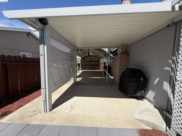 Covered patio area featuring a concrete slab, metal awning, and privacy screen
