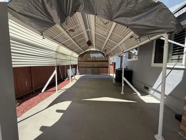 Covered carport structure with a concrete floor, corrugated metal roof, and a privacy screen