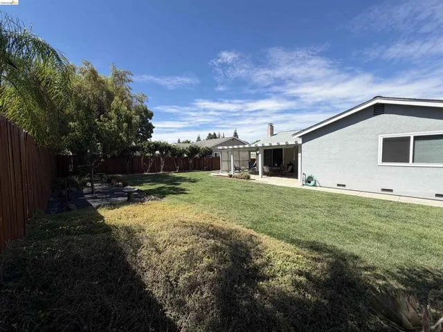 Expansive backyard featuring a lush lawn, a privacy fence, established trees, and a covered patio structure