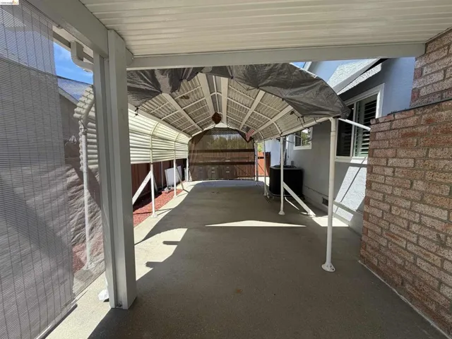 Covered carport featuring a concrete surface, brick exterior wall, and sun shade