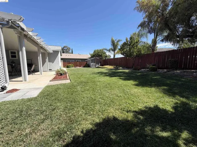 Expansive grassy yard featuring a concrete patio, a pergola-covered outdoor space, and a wood privacy fence