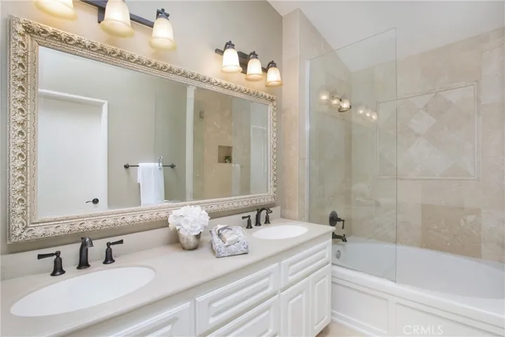 Primary bath with stone counters and tub/shower surround, frameless glass doors