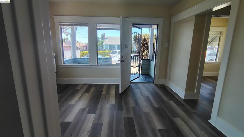Spacious interior featuring wide plank wood-finish flooring, a front entry door with a security screen, and multiple windows with white trim