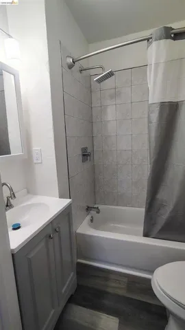 Bathroom featuring a modern shower head, subway tile surround, white bathtub, gray vanity, and wood-finish flooring