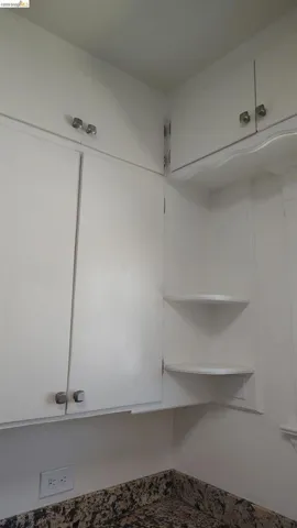White upper cabinetry with brushed nickel hardware, built-in corner shelving, and granite-look countertops