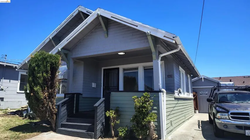 Craftsman-style exterior featuring a covered porch with dark-stained railings and steps, horizontal siding in two tones, visible eaves with decorative brackets, and white-framed windows