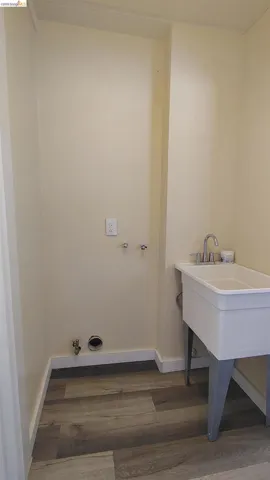 Dedicated laundry area featuring wood-finish flooring, light-toned walls, and white baseboards