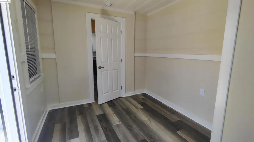 Interior room featuring wood-finish flooring, light-toned walls with wainscoting, white trim, and a white interior door